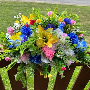 May include: A colourful artificial flower arrangement with pink, white, yellow, blue, and green flowers. The arrangement is on a wooden fence.