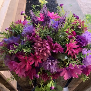 May include: A vibrant purple and pink flower arrangement with green foliage. The flowers are arranged in a circular shape and are perfect for a spring or summer decor.