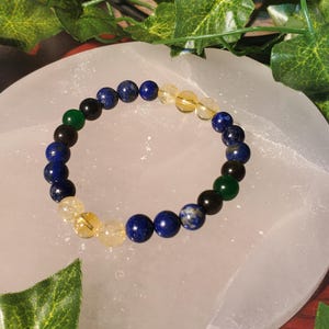 May include: A bracelet made of blue, green, black, and yellow beads. The bracelet is on a white surface.