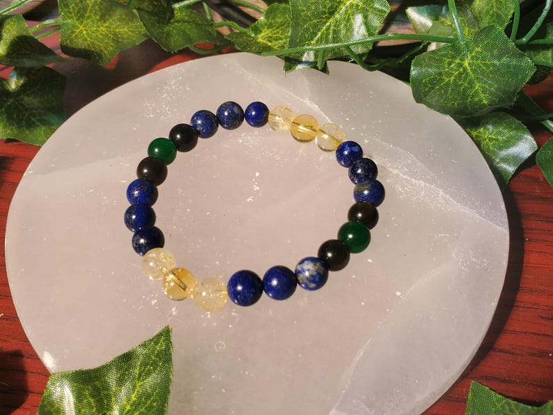 May include: A bracelet made of blue, green, black, and yellow beads. The bracelet is on a white surface.