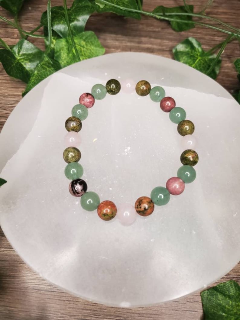 Peut inclure: Un bracelet compos&eacute; de perles de pierres pr&eacute;cieuses vertes, roses et brunes. Le bracelet est sur une surface blanche.