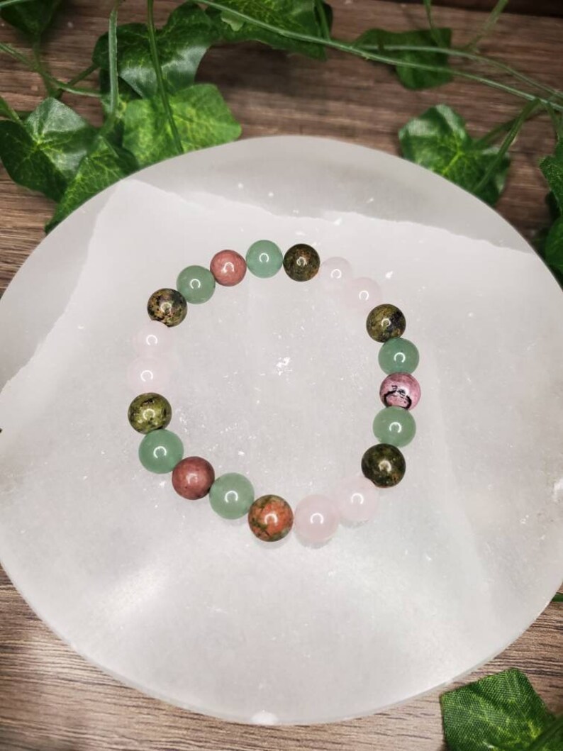 Peut inclure: Un bracelet compos&eacute; de perles de pierres pr&eacute;cieuses vertes, roses et brunes. Le bracelet est sur une surface blanche.