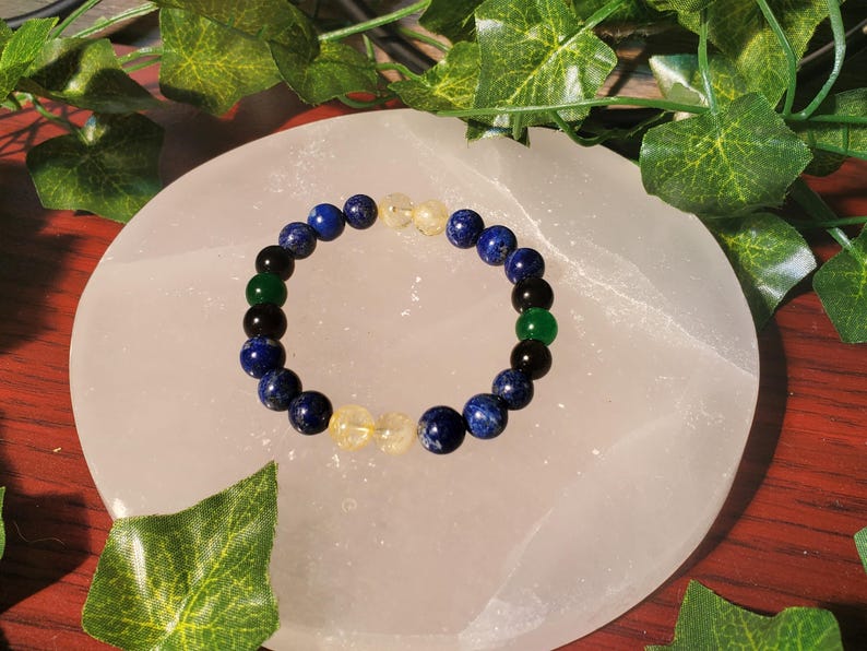 May include: A bracelet made of blue, green, black, and yellow beads. The bracelet is on a white surface.