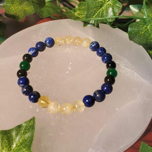 May include: A beaded bracelet with blue, green, and yellow stones. The bracelet is on a white surface.