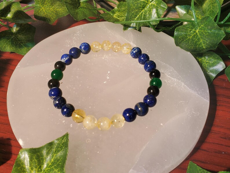 May include: A beaded bracelet with blue, green, and yellow stones. The bracelet is on a white surface.
