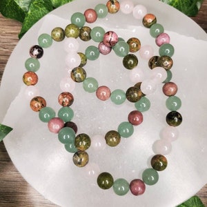 Peut inclure: Trois bracelets en perles avec des pierres vertes, roses et brunes. Les bracelets sont dispos&eacute;s sur une surface blanche.