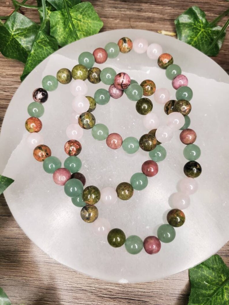 Peut inclure: Trois bracelets en perles avec des pierres vertes, roses et brunes. Les bracelets sont dispos&eacute;s sur une surface blanche.
