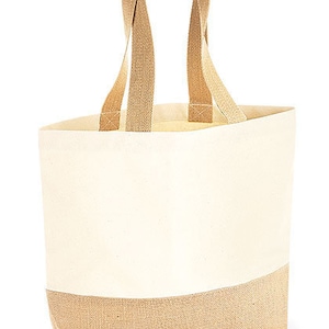 May include: Cream-colored tote bag with tan handles and a tan bottom. The bag has a rectangular shape and is made of a canvas-like material. The handles are wide and appear to be made of a woven fabric. The text "Tasche M" is printed on the bottom right.