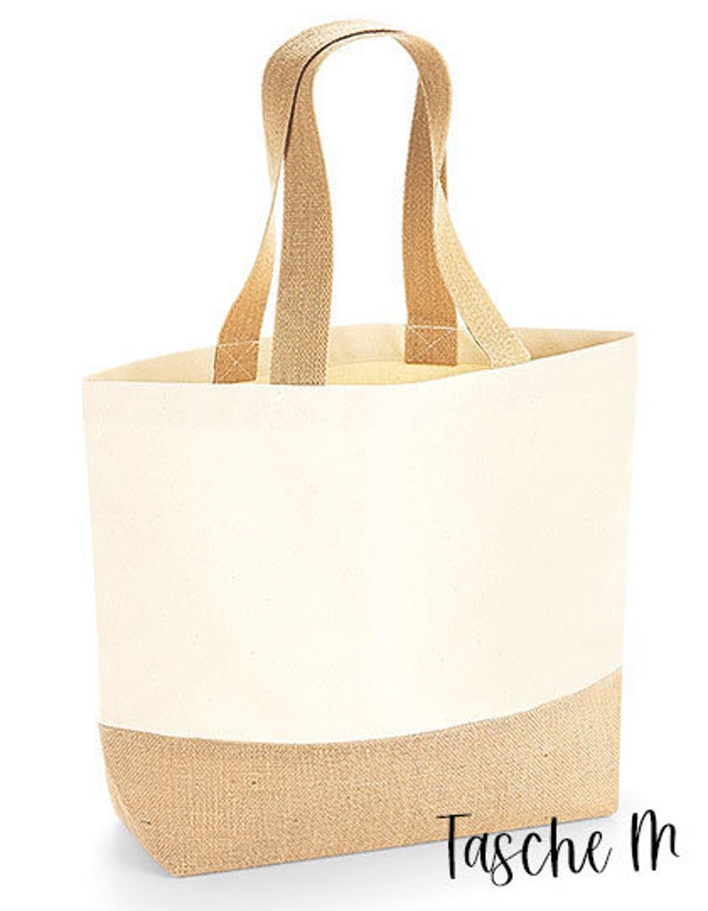 May include: Cream-colored tote bag with tan handles and a tan bottom. The bag has a rectangular shape and is made of a canvas-like material. The handles are wide and appear to be made of a woven fabric. The text "Tasche M" is printed on the bottom right.