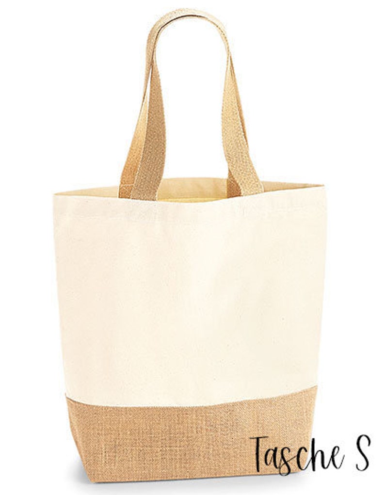 May include: A canvas tote bag with a natural beige color and a jute bottom. The bag has matching beige handles and the text "Tasche S" in a script font on the bottom right corner. The bag is designed for carrying items.