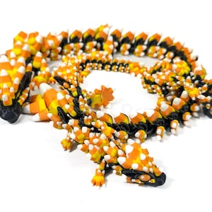 May include: A 3D-printed dragon sculpture in the shape of candy corn. The dragon is primarily orange, yellow, white, and black. The body is segmented, and the head and tail are detailed. A unique Halloween decoration.