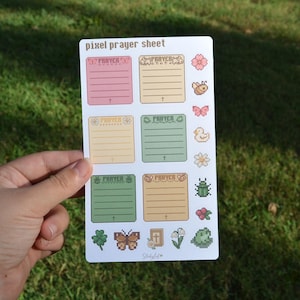 May include: A white sticker sheet titled pixel prayer sheet featuring six rectangular boxes with lined sections for writing, each labeled prayer. The sheet includes pixel art icons of a flower, bee, butterfly, duck, daisy, beetle, berries, clover, moth, bible, and frog.