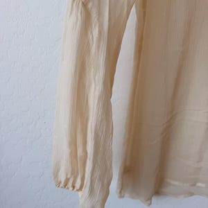 K&ouml;nnte beinhalten: Cremefarbene Bluse mit langen &Auml;rmeln aus strukturiertem, halbtransparentem Stoff. Der &Auml;rmel hat eine geraffte Schulterpartie und ein eng anliegendes B&uuml;ndchen. Die Bluse wirkt leicht und flie&szlig;end.