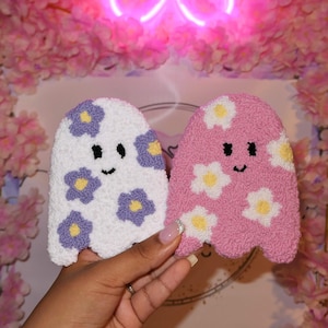 May include: Two plush ghost ornaments with embroidered flower designs. One ghost is white with purple flowers and the other is pink with yellow flowers.