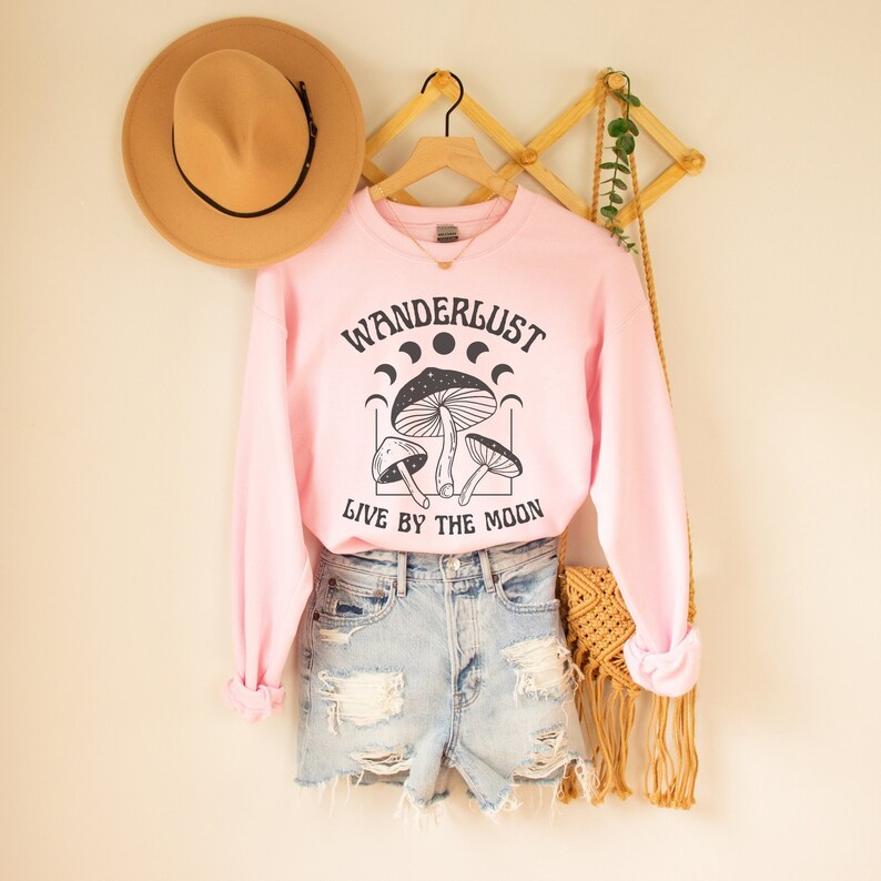 May include: Pink sweatshirt with a black graphic of mushrooms and the text "Wanderlust Live by the Moon".