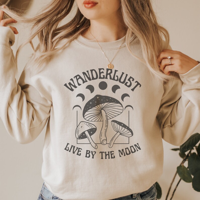 May include: A cream-colored sweatshirt with the text "Wanderlust Live by the Moon" and a graphic of three mushrooms with crescent moons and stars.