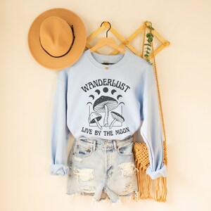 May include: Light blue sweatshirt with a graphic of mushrooms and moons and the text "Wanderlust Live by the Moon".