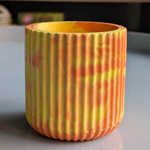 Peut inclure: Pot cylindrique à l'extérieur cannelé, peint en jaune et orange avec un effet marbré. L'intérieur est jaune uni. Ce pot décoratif convient à l'intérieur ou à l'extérieur. Le design évoque un coucher de soleil.