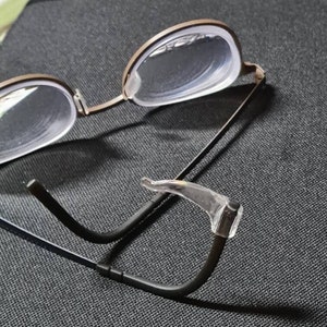 Peut inclure: Une paire de lunettes noires avec des verres transparents et un nez en plastique transparent. Les lunettes sont pliées en deux et le nez est visible.