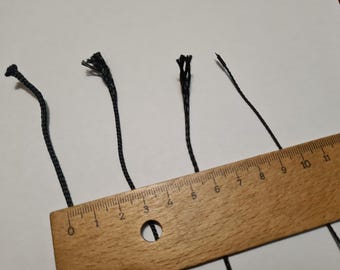 May include: Four black cords with frayed ends are lined up on a wooden ruler with markings in inches. The ruler is marked from 0 to 12 inches.
