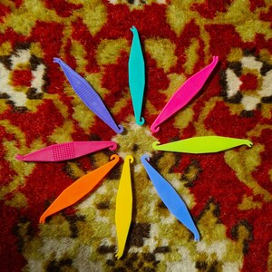 Può includere: Otto elastici per capelli in plastica colorati disposti a forma di stella su un tappeto a motivi. Gli elastici per capelli sono in tonalità di rosa, blu, verde, giallo e arancione.