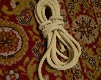 May include: A coiled length of off-white rope, likely cotton, lying on a patterned rug. The rope is thick and appears to be braided.