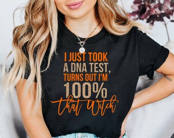 May include: Black t-shirt with the text "I JUST TOOK A DNA TEST, TURNS OUT I'M 100% that Witch" in orange and gold lettering. The shirt is a crew neck and is being worn.
