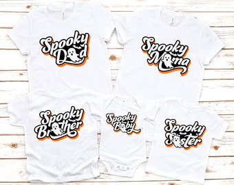 May include: White t-shirts and a onesie with the words "Spooky Dad", "Spooky Mama", "Spooky Brother", "Spooky Baby", and "Spooky Sister" in a black, orange, and white design. Each shirt features a ghost graphic, perfect for Halloween.
