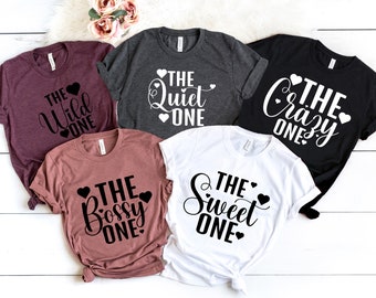 May include: Five t-shirts with different text and heart designs. The shirts are maroon, grey, black, pink, and white. The text on the shirts reads "The Wild One", "The Quiet One", "The Crazy One", "The Bossy One", and "The Sweet One".