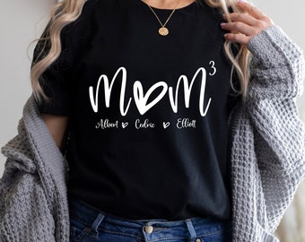 May include: Black t-shirt with white text that reads "mom³" with three hearts and the names "Albert", "Cedric", and "Elliott" underneath.