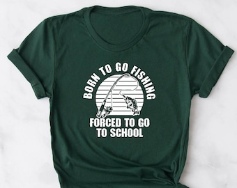 Op de afbeelding: Een donkergroen T-shirt met een witte afbeelding waarop staat "Born to go fishing, forced to go to school". De afbeelding bevat een zonsondergang en een hengel met een vis.
