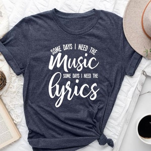 May include: A heather navy blue t-shirt with white text that reads "Some days I need the music, some days I need the lyrics."