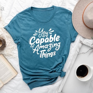May include: A teal blue t-shirt with the text "You are Capable of Amazing Things" in white lettering.