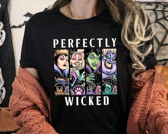 May include: Black t-shirt with the text "PERFECTLY WICKED" and a graphic of five cartoon villains. The shirt is worn with a rust-colored cardigan and black pants. A skull-patterned blanket and Halloween decorations are in the background.