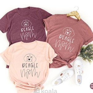 May include: Three t-shirts with the text "BEAGLE MOM" in black script and a line drawing of a beagle dog's head. The shirts are in heather maroon and heather peach.