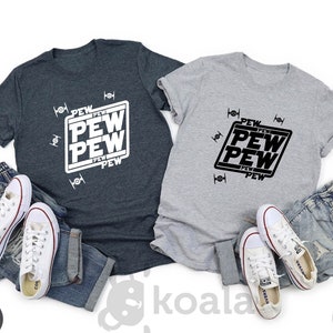 May include: Two t-shirts with the text "PEW PEW PEW" in a box with a star wars inspired design. The shirts are in dark heather gray and light gray.