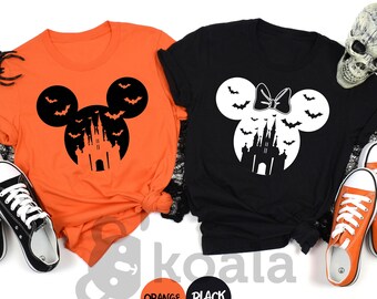 May include: Two Halloween-themed t-shirts, one orange and one black, featuring a Mickey Mouse silhouette with a castle and bats design. The orange shirt has a black design, while the black shirt has a white design. Black and white sneakers and orange sneakers are placed near the shirts.