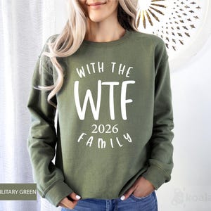 A woman wearing a green sweatshirt with the text "WTF 2026 FAMILY" printed on it.
