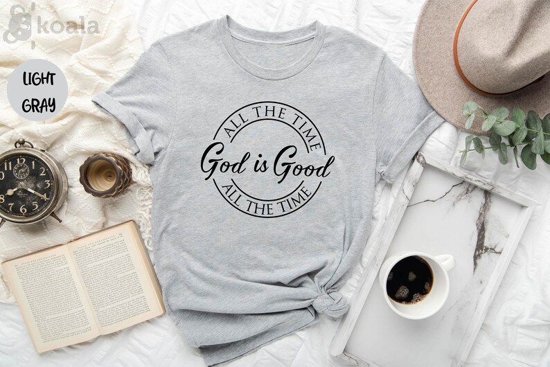Puede incluir: Una camiseta gris claro con un gr&aacute;fico circular negro que dice "All the time God is Good All the time".