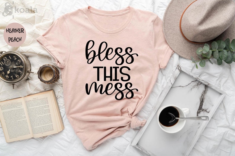 Puede incluir: Una camiseta rosa con el texto "bless this mess" en letras negras.
