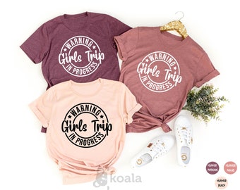 May include: Three t-shirts with the text "WARNING Girls Trip IN PROGRESS" in a circle. The shirts are in heather maroon and heather peach.