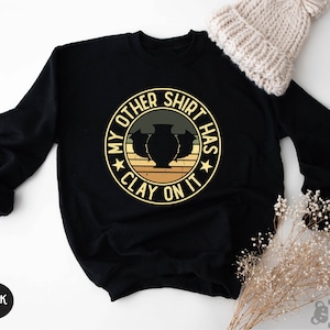 May include: Black sweatshirt with a vintage-style graphic that says "My other shirt has clay on it". The graphic features a star, three clay pots, and a striped background.