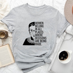 May include: Light gray t-shirt with a black and white illustration of Ruth Bader Ginsburg and the text "Women belong in all places where decisions are being made."