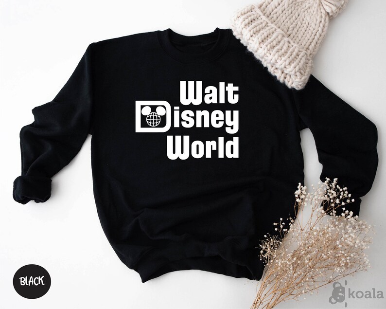 May include: Black sweatshirt with the words "Walt Disney World" in white block letters. The design includes a Mickey Mouse head and a globe. A white knit beanie and dried flowers are in the background. The word "BLACK" is in a black circle.