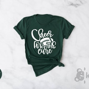 May include: A dark green t-shirt with the text "Cheer for the cure" in white lettering and a white football graphic.