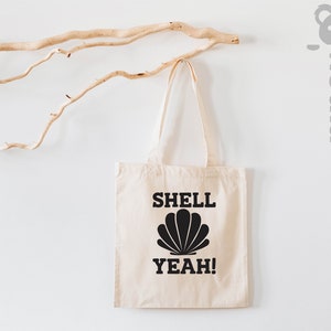 May include: A white canvas tote bag with black text that reads "SHELL YEAH!" and a black seashell graphic.