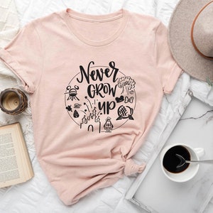 May include: A pink t-shirt with the text "Never Grow Up" in a circle with black and white illustrations of Disney characters and attractions.