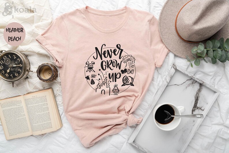 May include: A pink t-shirt with the text "Never Grow Up" in a circle with black and white illustrations of Disney characters and attractions.