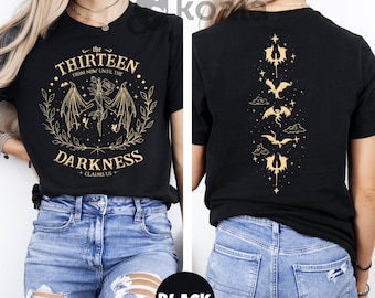 May include: Black t-shirt with a gold graphic design featuring the text "the thirteen from now until the darkness claims us" and a winged creature. The back of the shirt has a vertical design of five winged creatures and stars.
