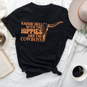 May include: Black t-shirt with a graphic of a cow skull and the text "Raisin' Hell With The Hippies And The Cowboys".
